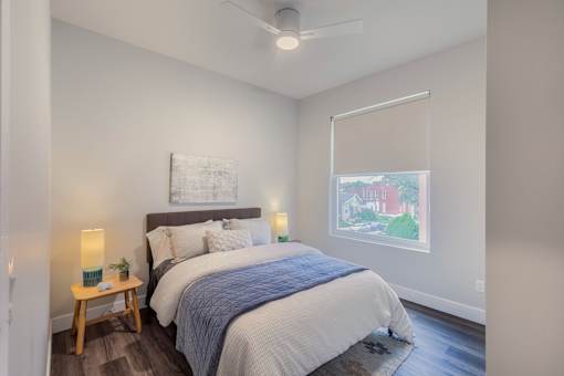 A bedroom with a bed, a nightstand with a lamp, and a painting on the wall.