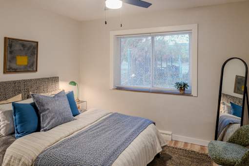 A bedroom with a bed, pillows, a ceiling fan, and a window with blinds.