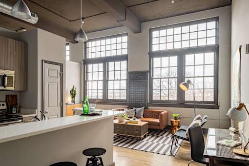A modern kitchen with a bar stool and a table with a lamp.