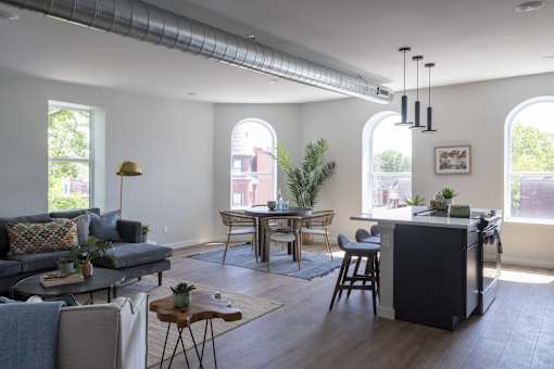 A modern living room with a grey couch, a wooden coffee table, and a kitchen area with a black fridge.