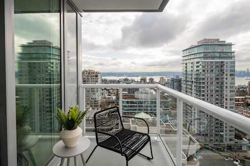 A balcony with a chair and a potted plant overlooking a cityscape.