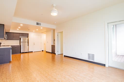 an empty living room with wood flooring and a kitchen