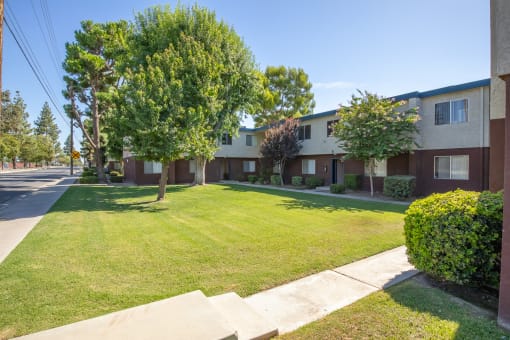 an apartment building with a lawn and trees in front of it