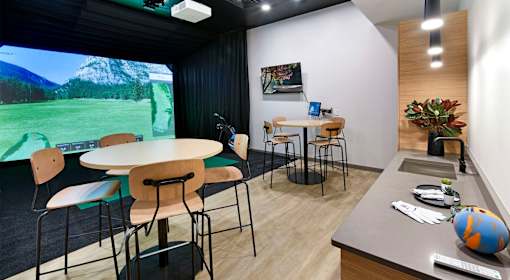 A room with a table, chairs, and a large screen displaying a mountainous landscape.