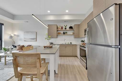 A modern kitchen with a stainless steel refrigerator and wooden chairs.
