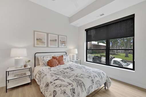 A bedroom with a large bed and a window showing a car and trees outside.