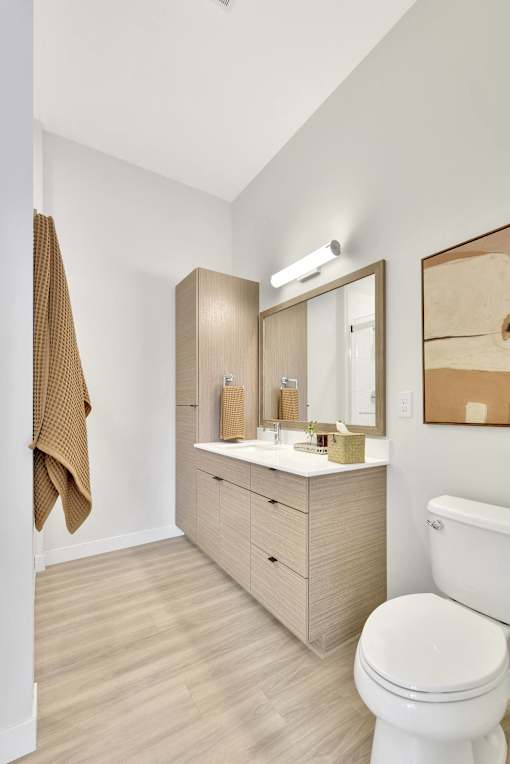 A white toilet sits in a bathroom with a wooden vanity and a mirror.