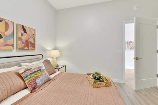 A bedroom with a bed, two lamps, a basket of flowers, and two paintings on the wall.
