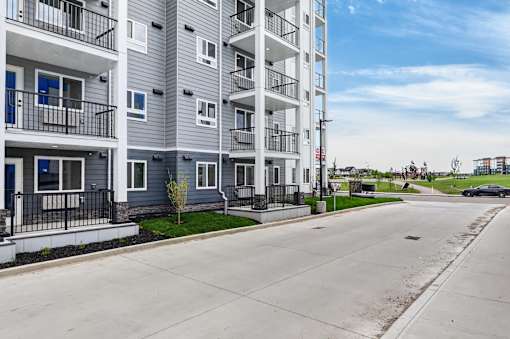 A street view of a residential area with apartment buildings on the left and a car parked on the right.