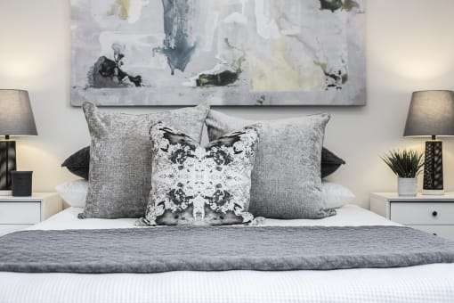 a bedroom with a bed with grey and white bedding and two paintings on the wall