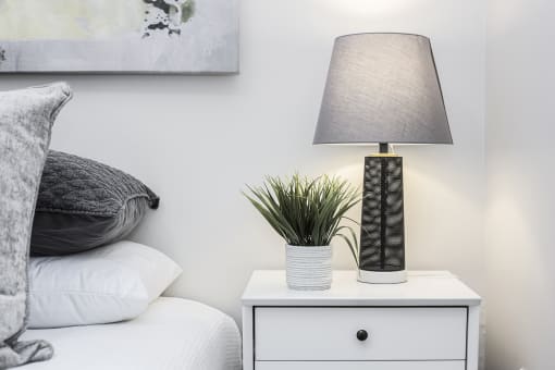 a bedroom with a bedside table with a lamp and a plant on top of it
