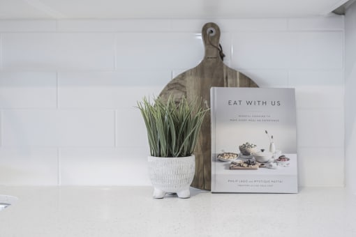 the book eat with us sits on a counter next to a vase with a plant