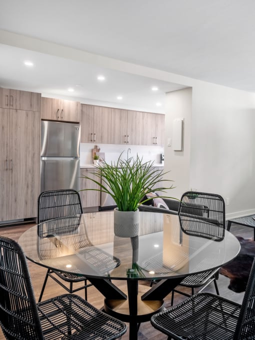 a dining area with a glass table and chairs and a kitchen in the background