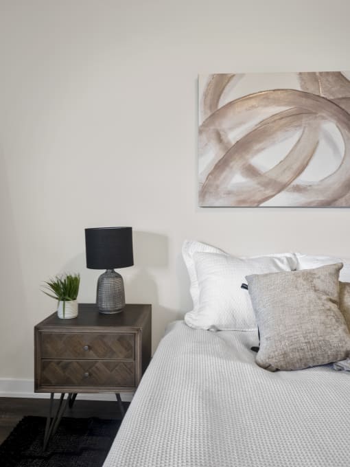 a bedroom with white bedding and a brown nightstand with a lamp and a plant