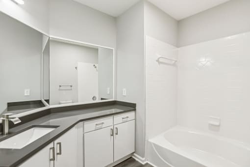 A white bathroom with a sink, mirror, and bathtub.