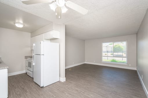 an empty living room with a kitchen in the background