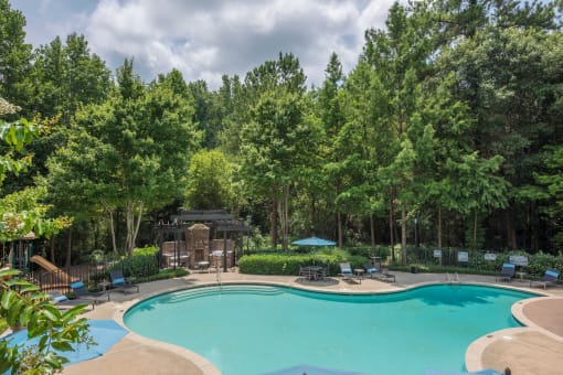a swimming pool with chairs around it and trees in the background
