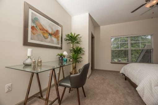 a bedroom with a bed and a glass desk with a chair