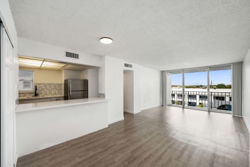 the living room and kitchen of an apartment with wood flooring and a large window