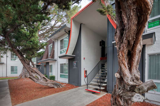 a building with a gray and red exterior and two large trees in front of it