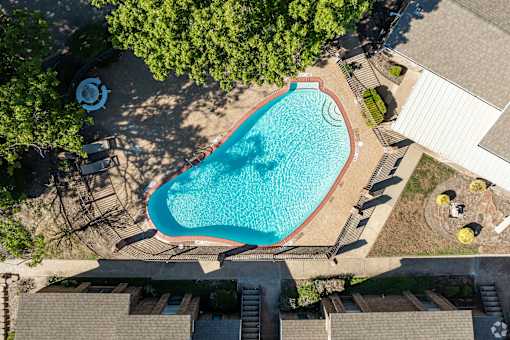 An aerial view of a swimming pool surrounded by trees and buildings.