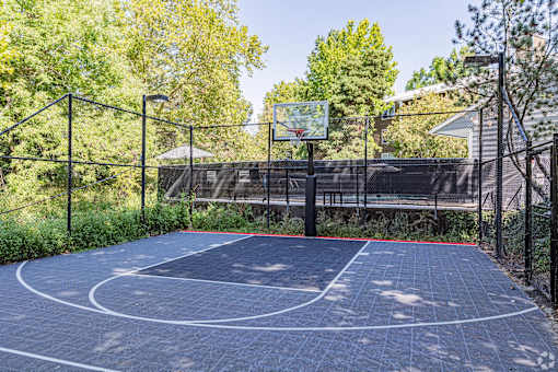 A basketball court surrounded by a fence with trees in the background.