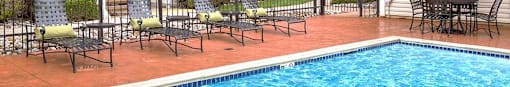 a swimming pool with chaise lounge chairs and umbrellas in front of a brick building