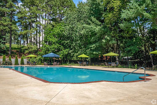 A large swimming pool surrounded by trees and umbrellas.