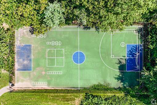 An aerial view of a green field with a basketball court and a tennis court.