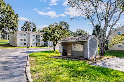 A small building sits in the middle of a grassy area with apartment buildings in the background.