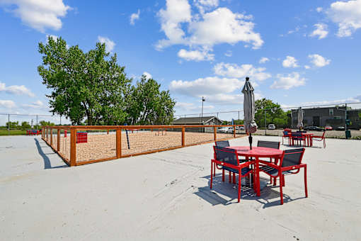 A table and chairs set up on a sandy surface with trees in the background.