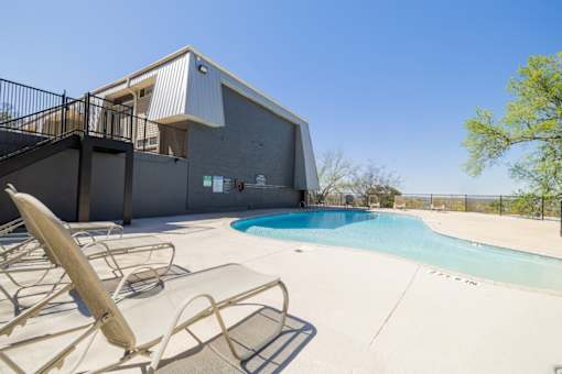 A pool with chairs and a building in the background.