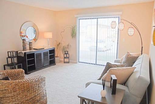 A living room with a grey couch, a wicker chair, a wooden cabinet with a mirror, and a small potted plant.