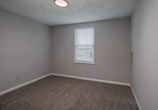 A room with a carpeted floor and a window with blinds.