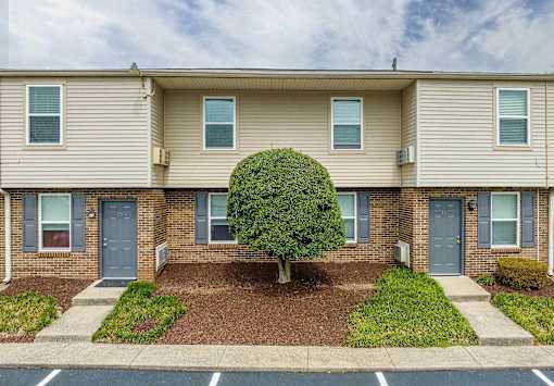 A beige apartment building with a tree in the front yard.
