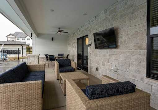 A patio with a couch, chairs, and a television mounted on a stone wall.