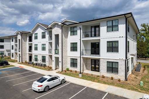 A white car is parked in a parking lot in front of a building.