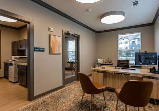 A room with a desk, chairs, and a window overlooking a city.