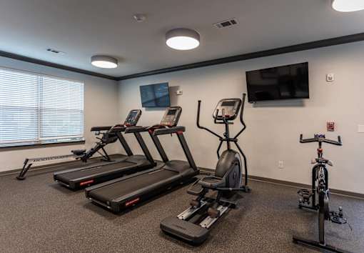 A gym with treadmills, exercise bikes, and a television.