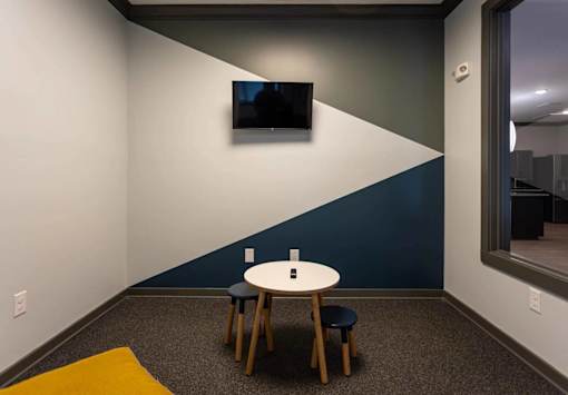 A room with a table and chairs and a television on the wall.