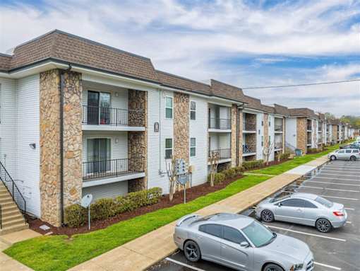 A row of apartment buildings with cars parked in front.