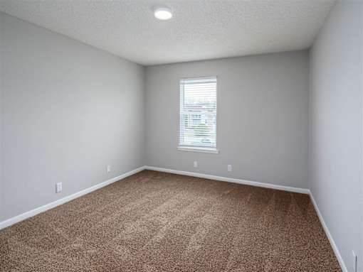 A room with a carpeted floor and a window with blinds.