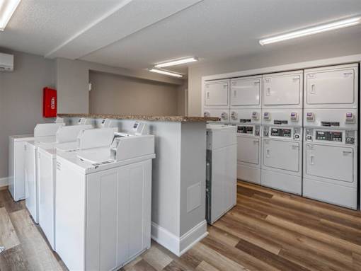 A laundry room with a washer and dryer on the left and a row of washers and dryers on the right.