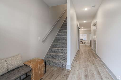 A long hallway with a staircase and a bench with a blanket on it.