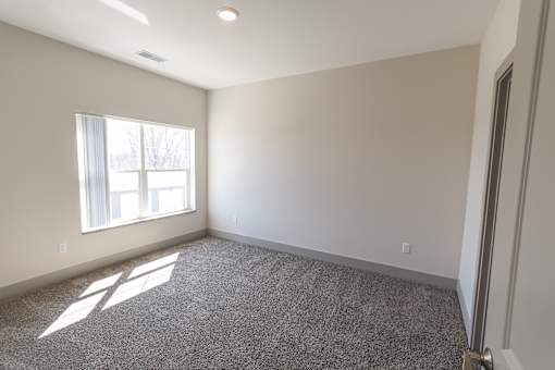 A room with a carpeted floor and a window letting in sunlight.