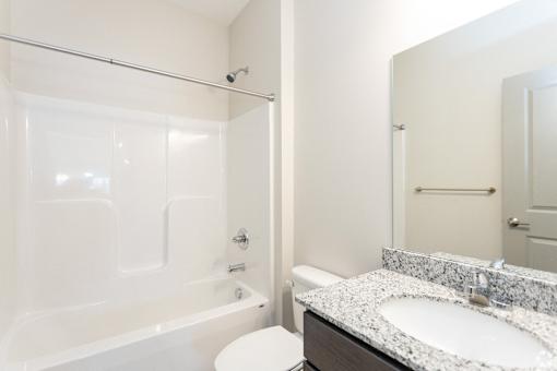 A white bathroom with a marble counter top and a white tub.