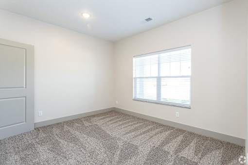 A room with a carpeted floor and a window with blinds.