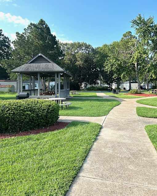 A gazebo is situated in a park with a paved walkway leading to it.