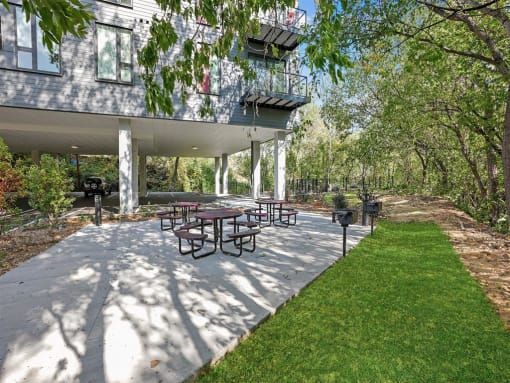 a patio with a grill and picnic tables in front of a building
