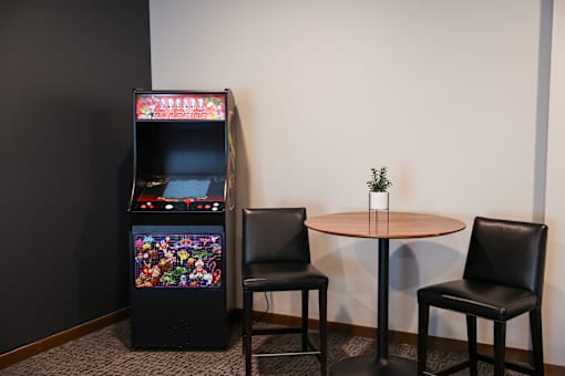 A small table with a plant on it sits between two chairs and a video game machine.